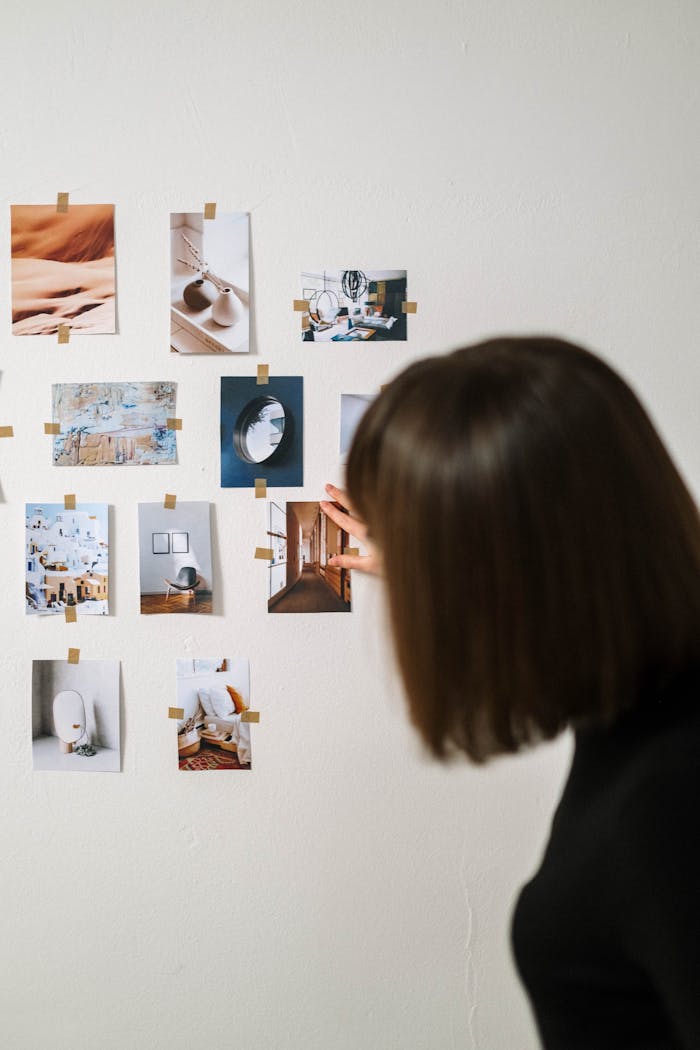 embark A woman arranges various art photographs on a light wall, creating a minimalistic display.